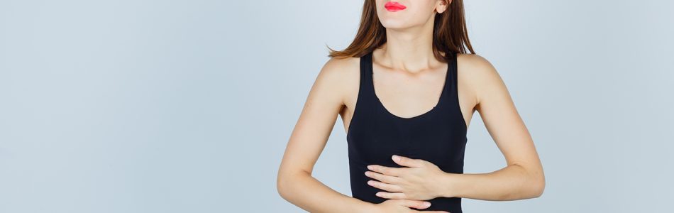 young lady suffering from stomachache in tank top, pants and looking painful. front view.