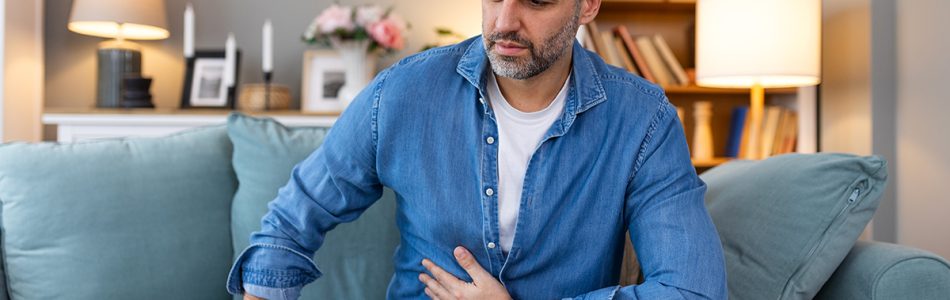 Terrible stomachache. Frustrated handsome young man hugging his belly and keeping eyes closed while lying on the couch at home