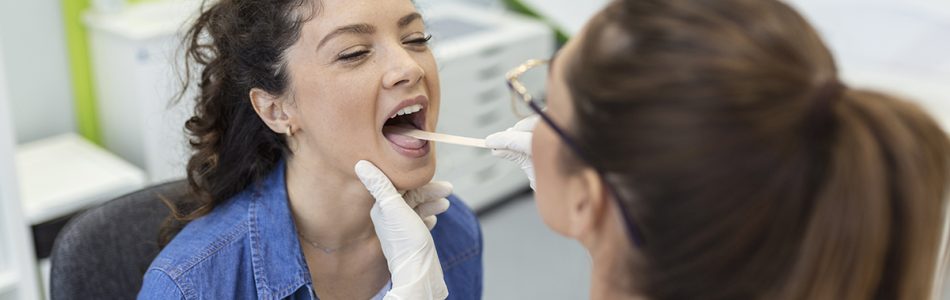 Female patient opening her mouth for the doctor to look in her throat. Otolaryngologist examines sore throat of patient.