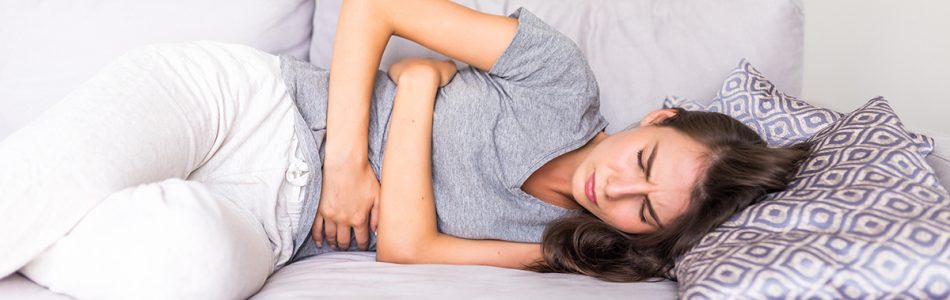 Women have abdominal pain because of menstruation lying in couch and holding her stomach.